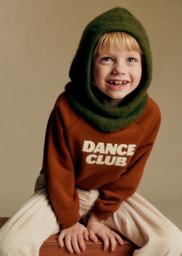 Ein Kind in einem roten Pulli mit einer Grünen Mütze auf