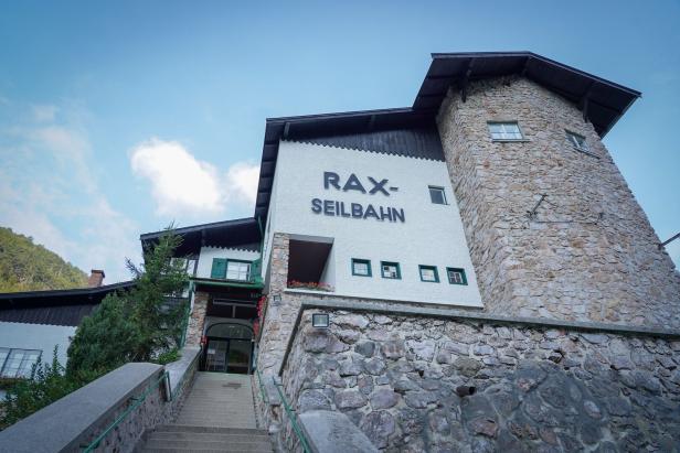 Steintreppen führen zu einem Gebäude mit der Aufschrift „Rax-Seilbahn“ und mehreren grünen Fenstern.