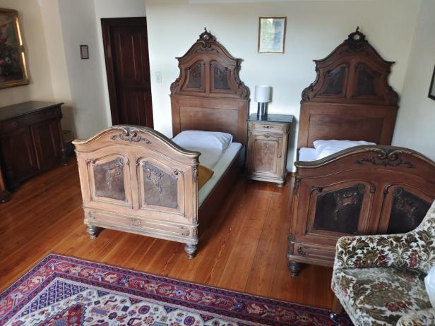 Zwei antike Einzelbetten mit verzierten Holzkopfteilen stehen nebeneinander in einem klassisch eingerichteten Zimmer.