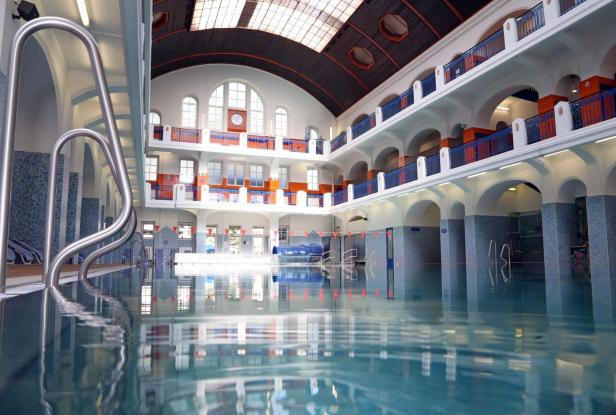 Hallenbad mit Schwimmbecken, Galerie und großer Fensterfront unter gewölbtem Dach.