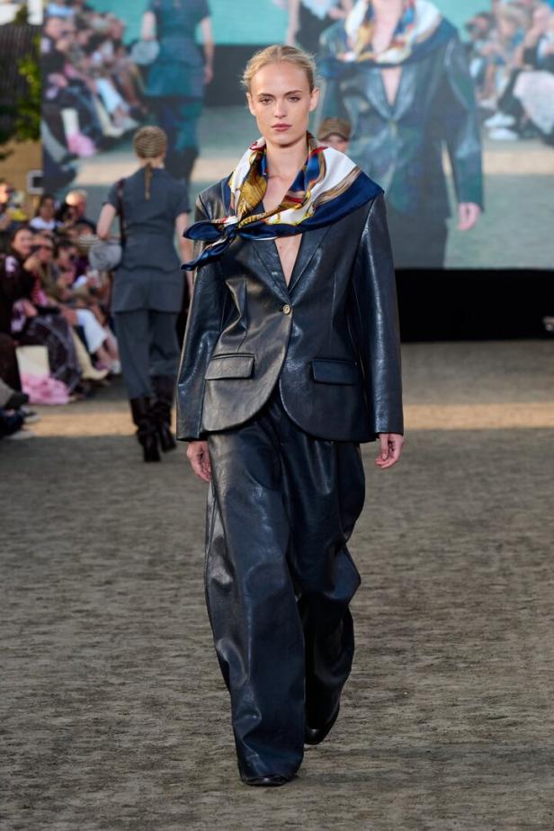 Eine Frau mit schwarzem Lederblazer und Lederhose und einem Tuch um den Hals gebunden 