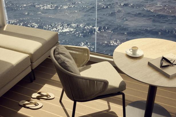 Elegante Lounge-Möbel auf einer Terrasse mit Meerblick, Kaffee, Buch und Sonnenbrille auf dem Tisch.