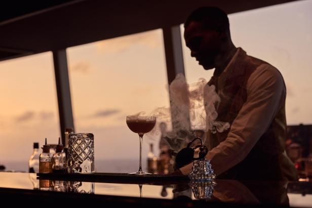 Barkeeper bereitet an einer Bar einen Cocktail vor Sonnenuntergang zu.