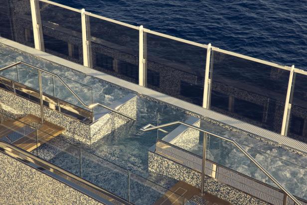 Whirlpool mit Mosaikfliesen an Deck eines Kreuzfahrtschiffs, dahinter Blick aufs Meer.