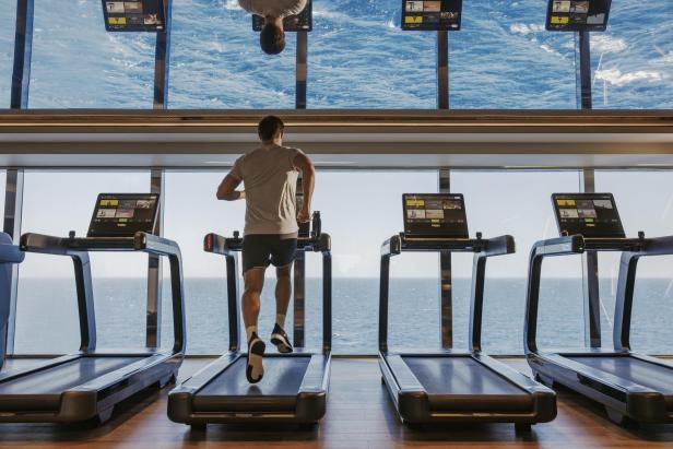 ein Mann läuft auf einem Laufband in einem Fitnessraum mit Meerblick auf einem Kreuzfahrtschiff.
