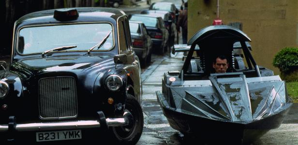 Ein schwarzes Taxi steht neben einem Mini-U-Boot, in dem Pierce Brosnan sitzt.
