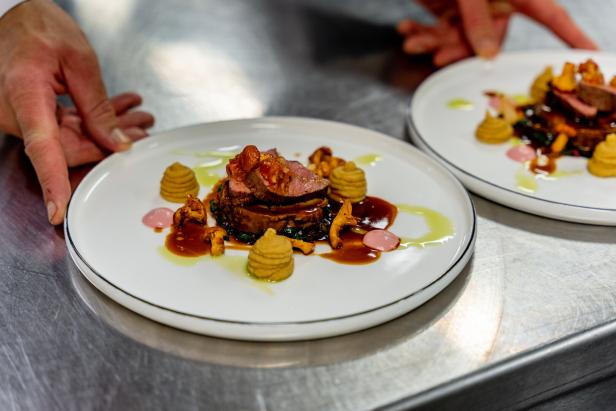 Ein kunstvoll angerichtetes Fleischgericht mit Pilzen, Soße, Püree-Tupfern und grüner Öldekoration auf einem weißen Teller.