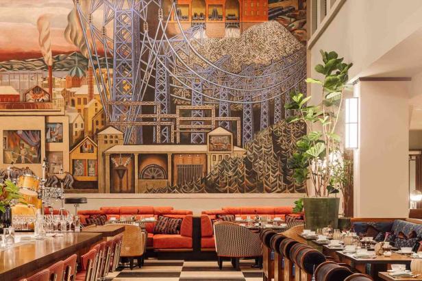 Ein stilvoll eingerichtetes Restaurant mit roten Sofas, gemusterten Stühlen und einer großen Wandmalerei mit Industrie- und Stadtmotiven.