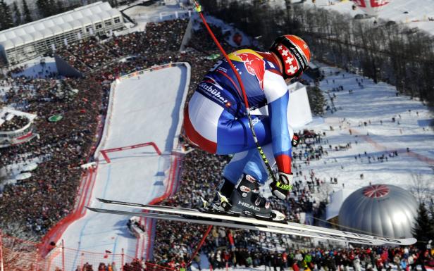 Ein Skirennfahrer springt in voller Ausrüstung über eine Skipiste vor einer großen Menschenmenge.