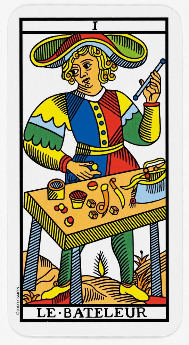 Eine Tarot-Karte: Ein Mann in bunter Kleidung steht am Tisch mit Würfeln und Bechern, darunter der Schriftzug "Le Bateleur".