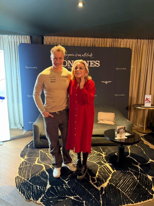 Isabella Klausnitzer mit Marco Odermatt stehen vor einer Couch und einem Longines-Werbeaufsteller. 