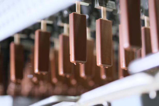 Eine Reihe von schokoladenüberzogenen Eis am Stiel hängt an einer Produktionslinie.