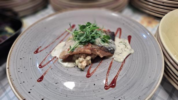 Ein Teller mit Lachs, garniert mit Kräutern und Saucen, steht bereit.