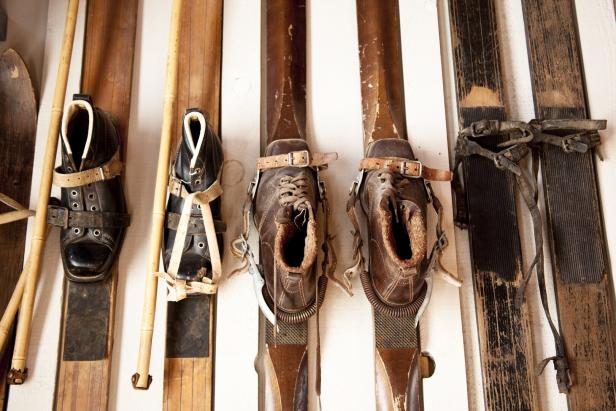 Mehrere Paar alte Skier mit dazugehörigen Lederschuhen und Stöcken sind nebeneinander angeordnet.