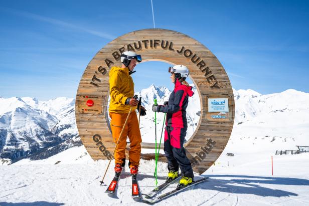 Zwei Skifahrer vor einer Holzkonstruktion mit der Aufschrift "It's a beautiful journey" in Heiligenblut.
