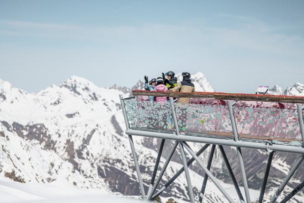 Eine Gruppe von Skifahrern steht auf einer Aussichtsplattform mit Blick auf schneebedeckte Berge.