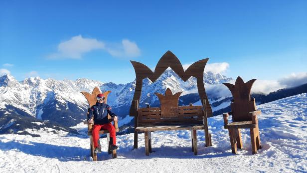 Ein Skifahrer sitzt auf einem Thron vor einer verschneiten Berglandschaft.