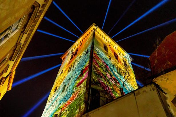Bunt beleuchteter Turm mit Lichtstrahlen am Nachthimmel während des Lichter-Festivals.