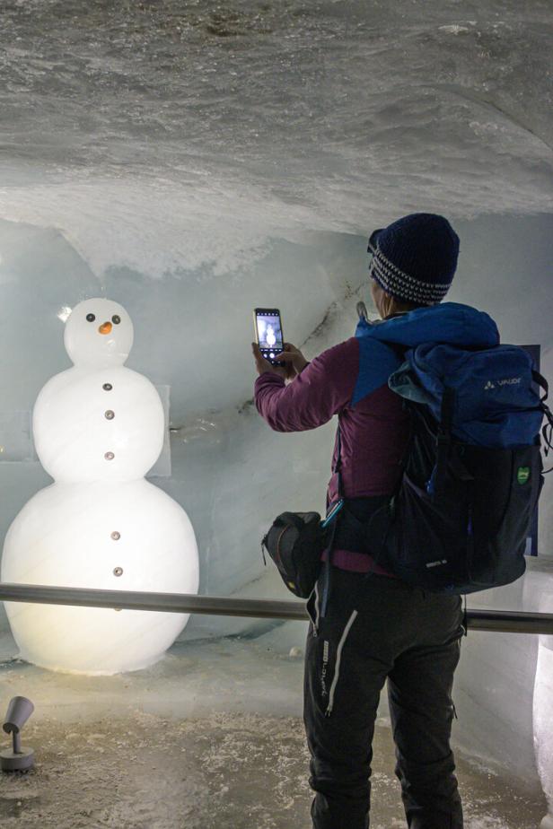 Eine Person mit Rucksack fotografiert einen Schneemann in einer Eisgrotte.