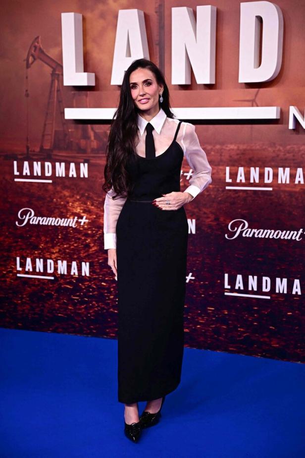 Demi Moore posiert bei einer Premiere in einem schwarzen Kleid mit Hemd und Krawatte.