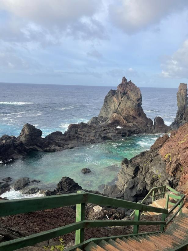 Treppe führt zu einer felsigen Küste mit türkisfarbenem Wasser und einem Felsenriff.