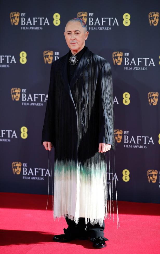 Alan Cumming im türkisweißen Rock und schwarzem Blazer.