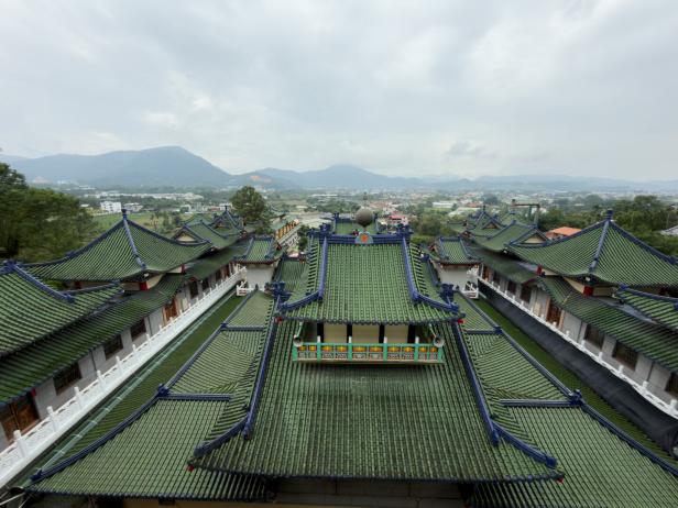 Grüne Dächer eines asiatischen Tempels erstrecken sich vor einer bergigen Landschaft.