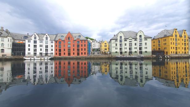 Bunte Häuserzeile in Ålesund spiegelt sich im Wasser.