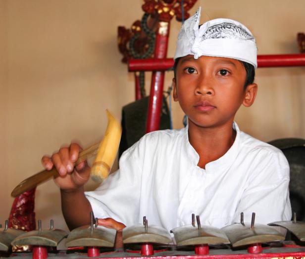 Ein Junge mit Kopfbedeckung spielt ein Musikinstrument mit einem Holzschlägel.