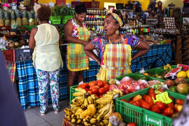 Auf einem Markt stehen Frauen hinter Ständen mit Obst und Gemüse.
