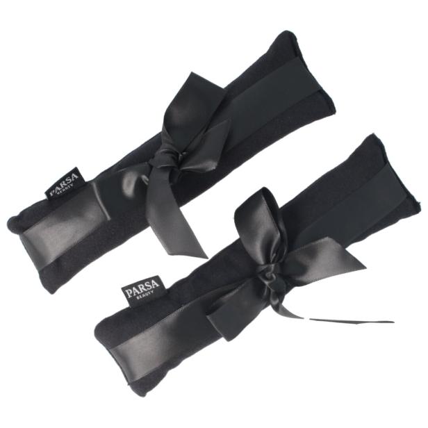 Zwei schwarze, bandumwickelte PARSA BEAUTY-Produkte mit Schleife liegen auf hellem Grund.