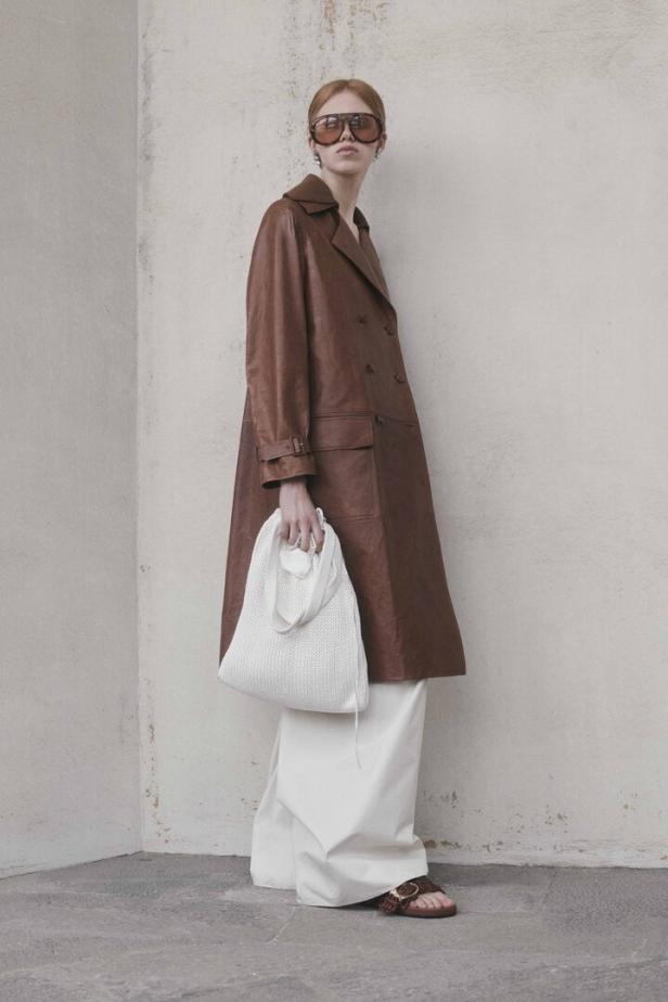 Frau in einem braunen Ledermantel mit weißer Hose