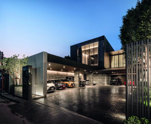 Modernes Haus mit großer Einfahrt, mehreren geparkten Autos und beleuchtetem Carport am Abend.