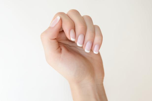 Eine Hand mit gepflegten Fingernägeln im French-Manicure-Stil vor hellem Hintergrund.