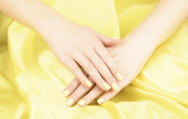Zwei Hände mit gelb lackierten Fingernägeln liegen auf gelbem Stoff.