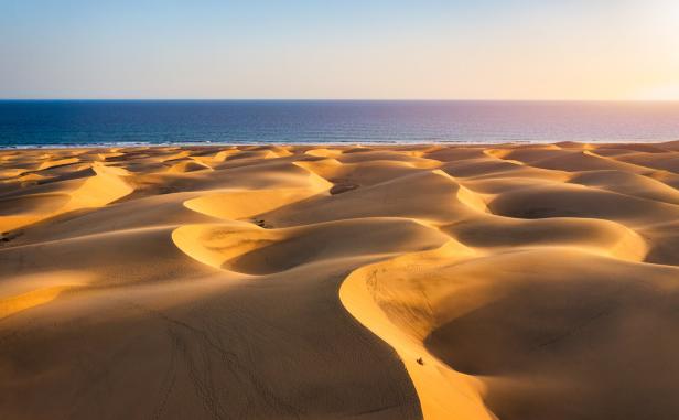 Weite goldene Sanddünen erstrecken sich bis zum blauen Meer unter klarem Himmel.