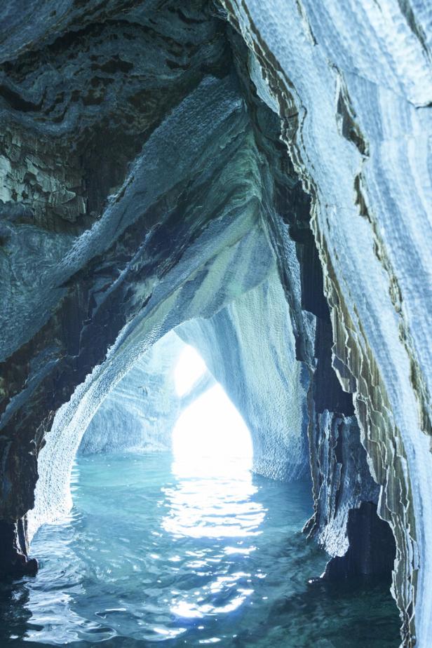 Höhle mit türkisfarbenem Wasser und von Licht durchfluteten, marmorierten Felswänden.