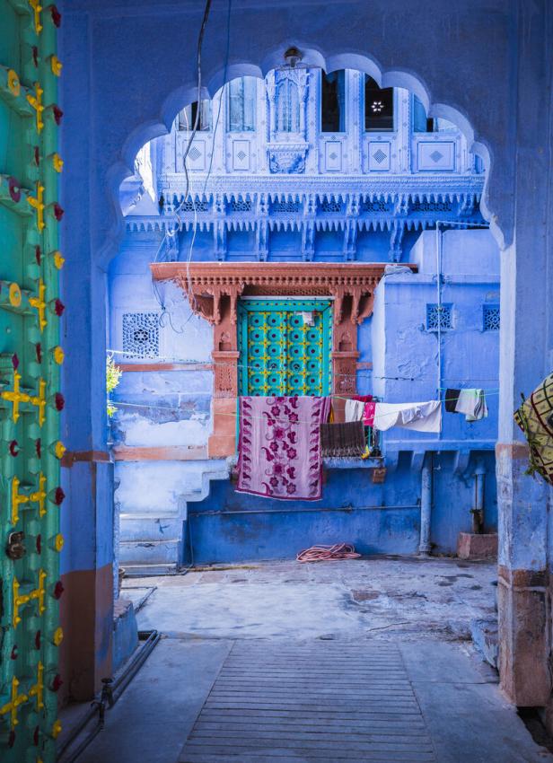 Blick durch einen Torbogen auf einen Innenhof mit blauen Wänden, bunter Tür und aufgehängter Wäsche.