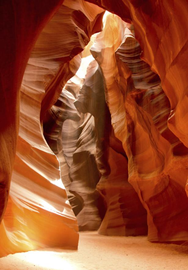 Sonnenlicht fällt durch die engen, geschwungenen Sandsteinwände einer rot-orangefarbenen Felsschlucht.