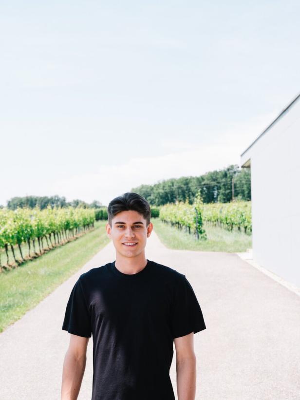 Ein Mann in schwarzem Shirt mit schwarzen Haaren vor einem Feld mit Weinreben