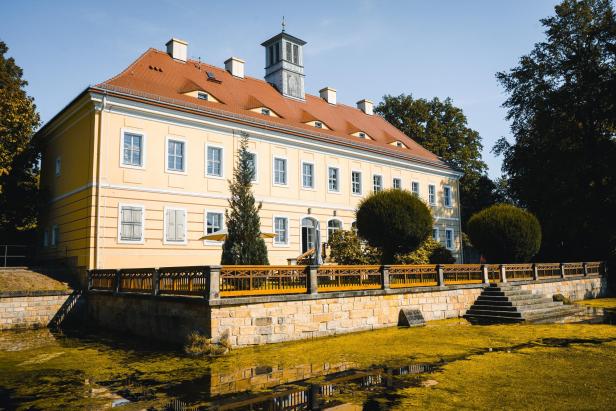 Gelbes barockes Schloss mit rotem Dach und Parkanlage bei sonnigem Wetter.
