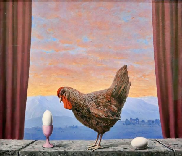 Eine braune Henne steht zwischen einem Ei im Eierbecher und einem Ei auf einer Mauer vor einem Sonnenuntergang.