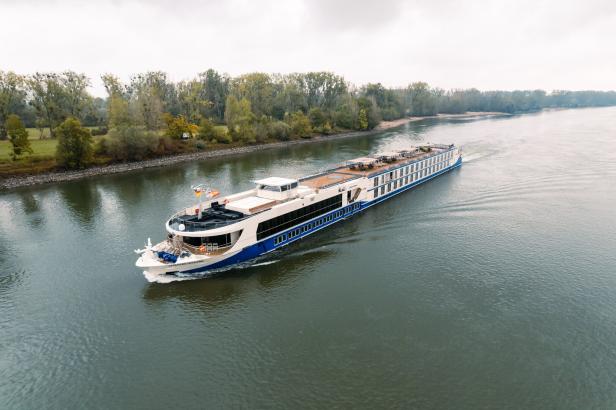Ein Flusskreuzfahrtschiff, die "Charles Dickens", fährt auf einem Fluss entlang bewaldeter Ufer.