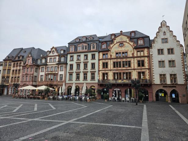 Mehrfarbige, historische Gebäude säumen einen gepflasterten Platz mit Cafés.