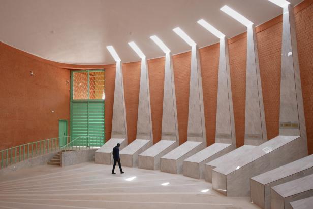 Eine Person geht durch einen großen, modernen Raum mit hohen, weißen Marmorsäulen und orangefarbener Backsteinwand.