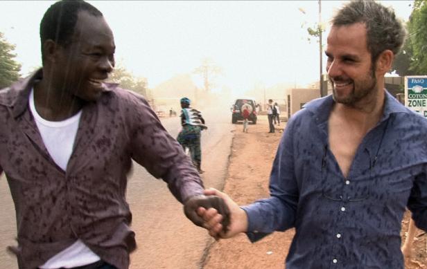 Zwei Männer laufen lachend Hand in Hand auf einer nassen Straße, während es regnet.