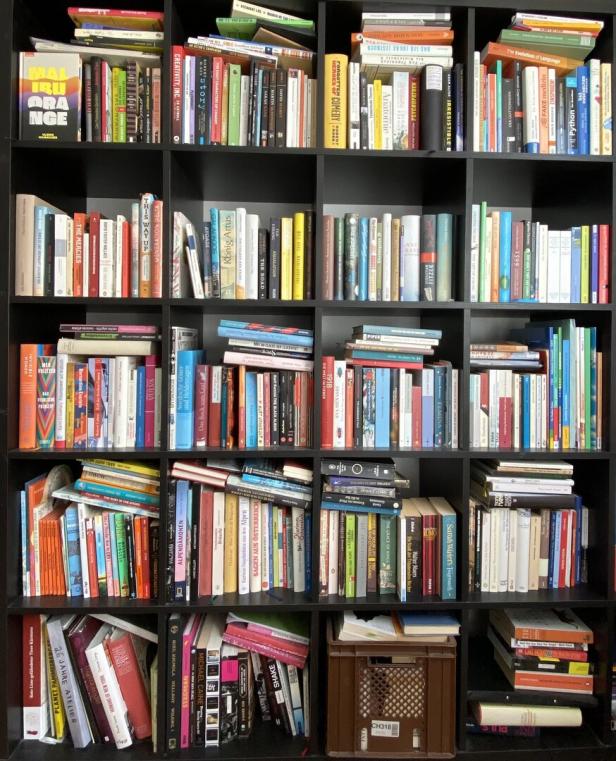 Ein großes, schwarzes Regal mit vielen Fächern, die unterschiedlich sortierte und gestapelte Bücher enthalten.