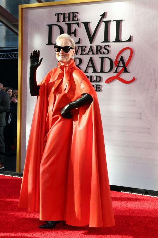 Meryl Streep,  mit Sonnenbrille, schwarzen Handschuhen und einem auffälligen roten Umhang am roten Teppich.