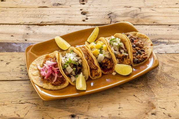 Clay tray with assorted Mexican tacos of cochinita pibil, pastor tacos, lime, chicken tinga,