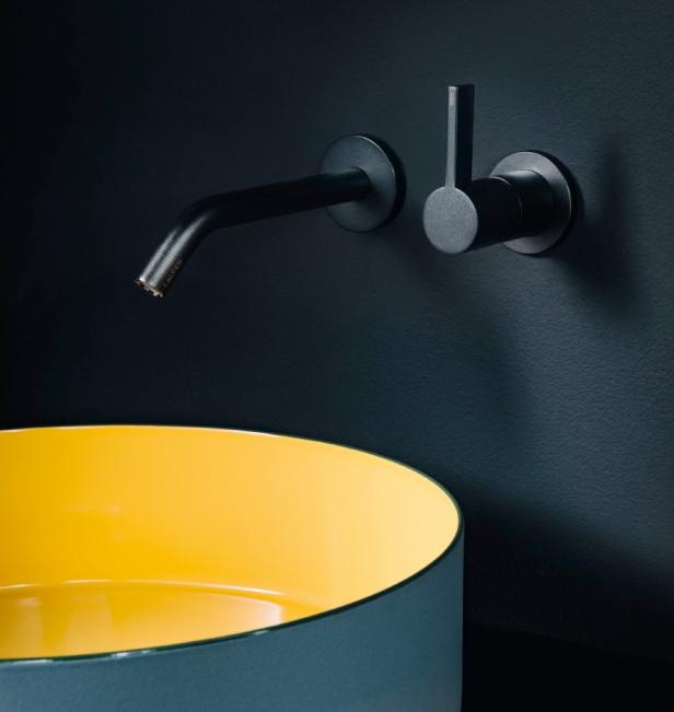 Ein gelb-blaues Waschbecken mit einer schwarzen Wand dahinter 